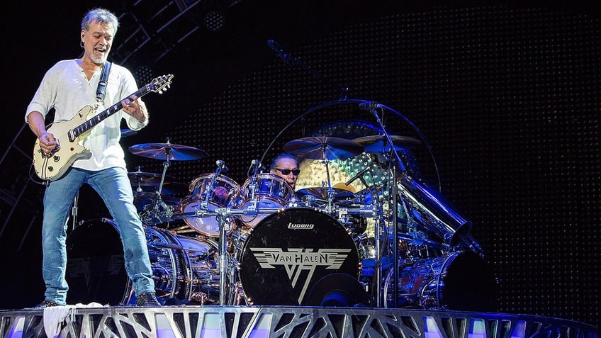 Eddie Van Halen playing guitar on stage with Alex Van Halen on drums behind him