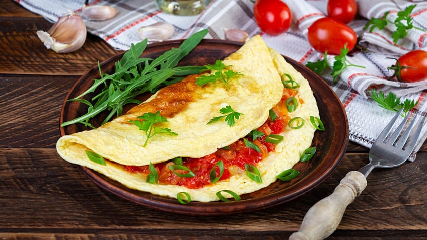 An omelet sits on a plate next to a fork on a table.