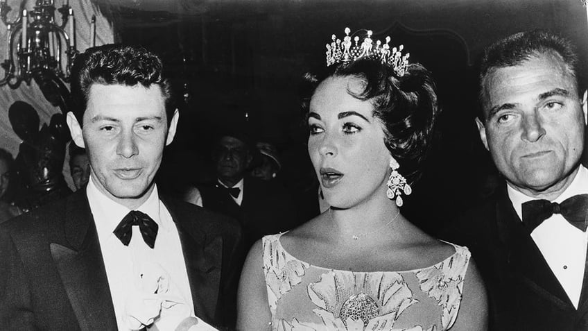 Elizabeth Taylor in a tiara walking in between Eddie Fisher and Mike Todd