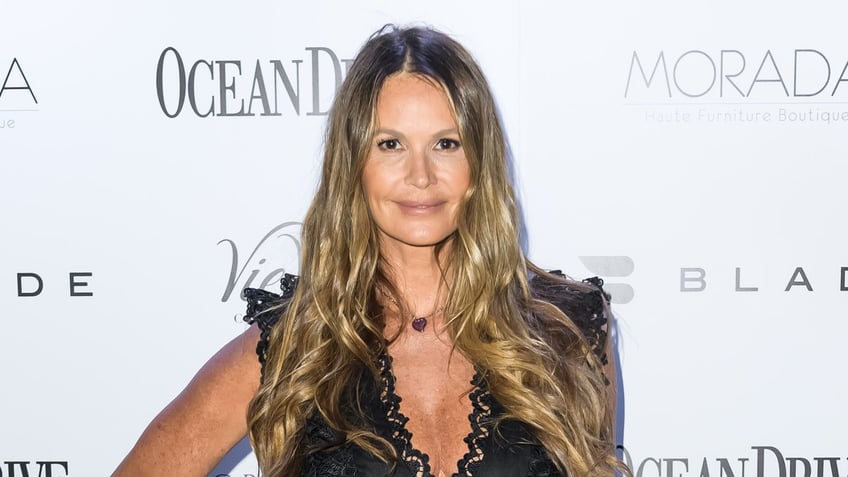 Elle Macpherson in a black lace plunging dress soft smiles ont he carpet