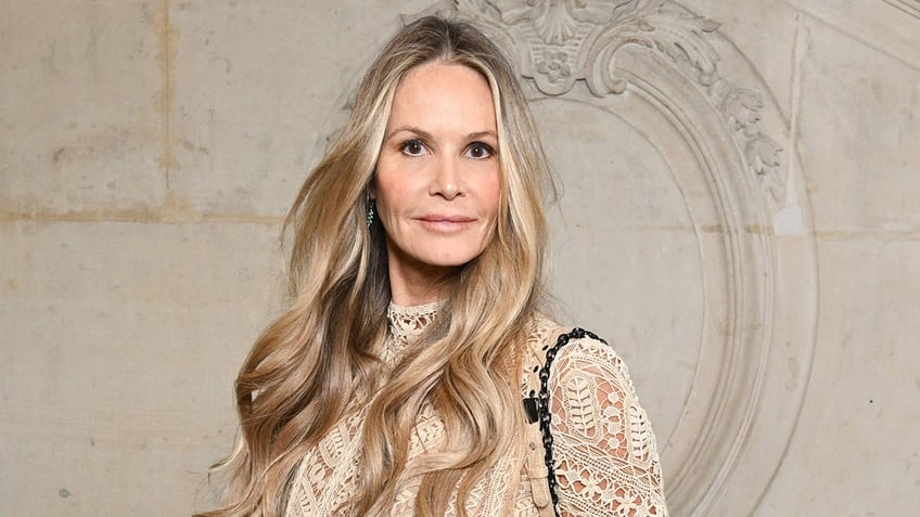 Elle Macpherson looks directly at the camera wearing a lace white outfit