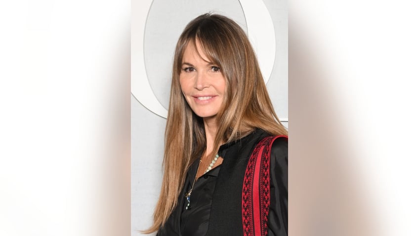 Elle Macpherson with dark brown hair in a black shirt holding a red bag