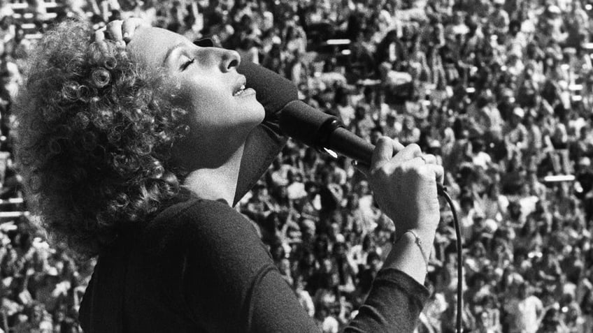 Barbra Streisand singing on stage in front of a large crowd.