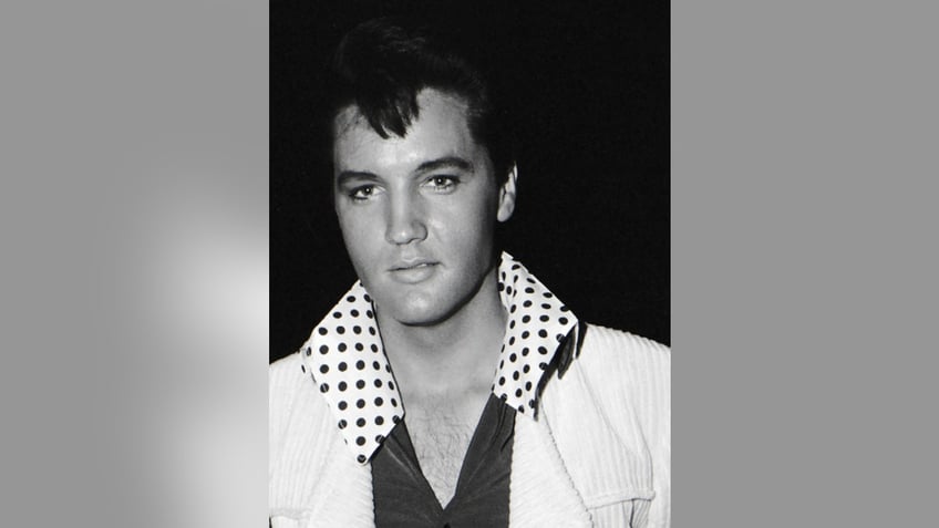 A close-up of Elvis Presley wearing a white blazer with a polka dot collared shirt.