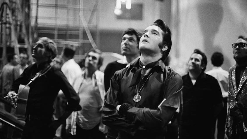 Elvis Presley looking up as hes surrounded by a crowd.