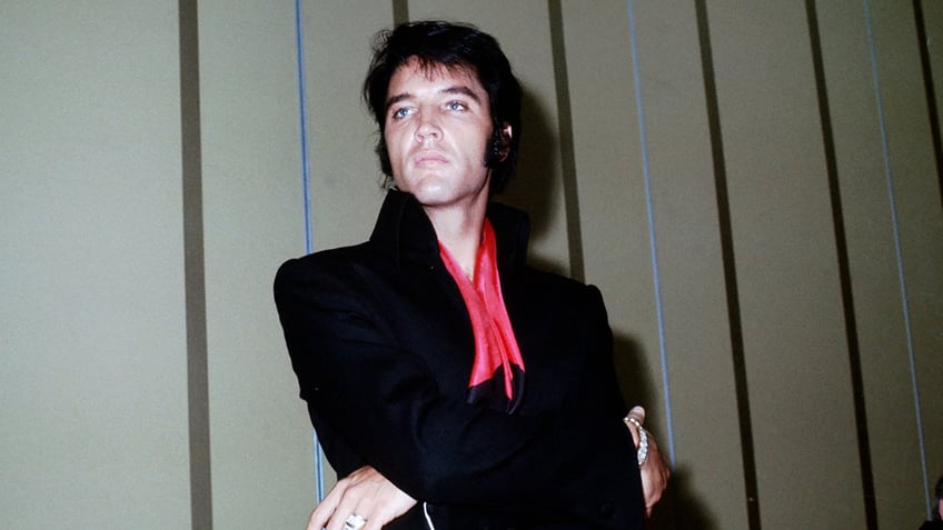 Elvis Presley wearing a black jumpsuit with a red scarf