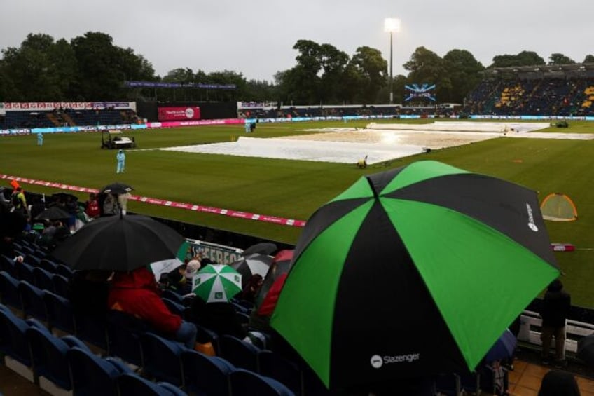 Wash out: Supporters sit under an umbrella in the stands at Cardiff's Sophia Gardens befor