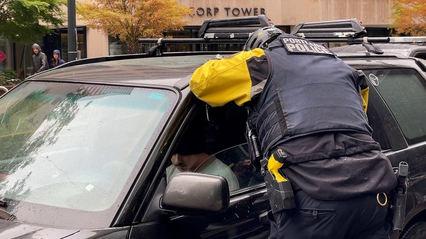 Police officer speaks to man sitting in driver's seat of a Subaru