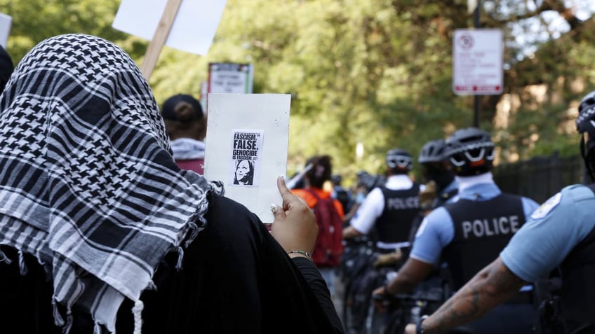 A anti-Israel protester at the Democratic National Convention holds a sign with a small picture of Vice President Kamala Harris next to the words, "Genocide is Fascism."