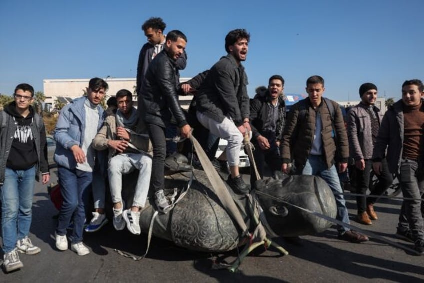 Damascus University students stand on a toppled statue of Syria's late president Hafez al-