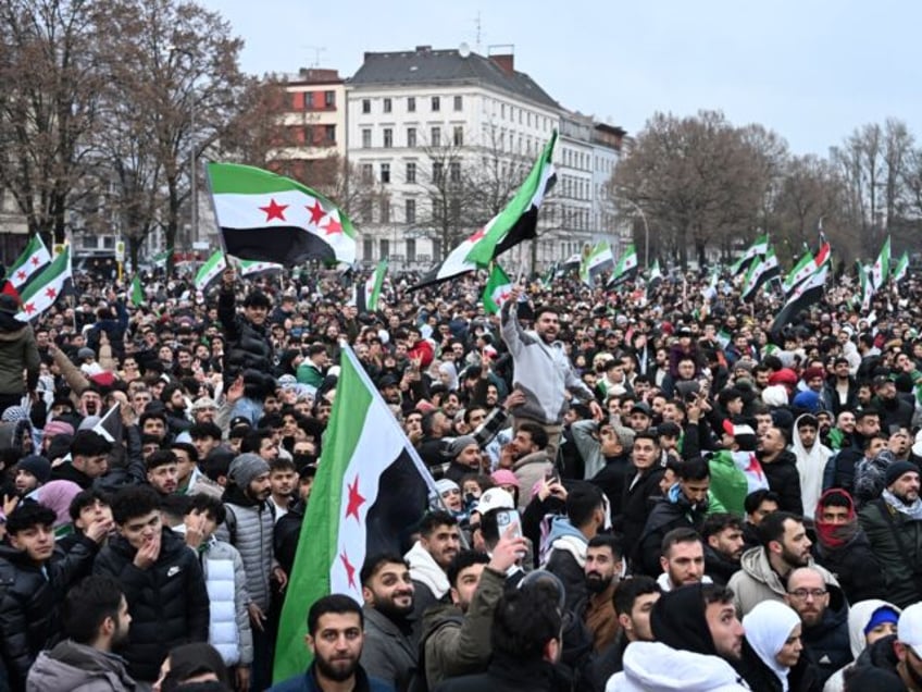 Members of the Syrian community wave Syrian flags as they attend a rally on December 8, 20