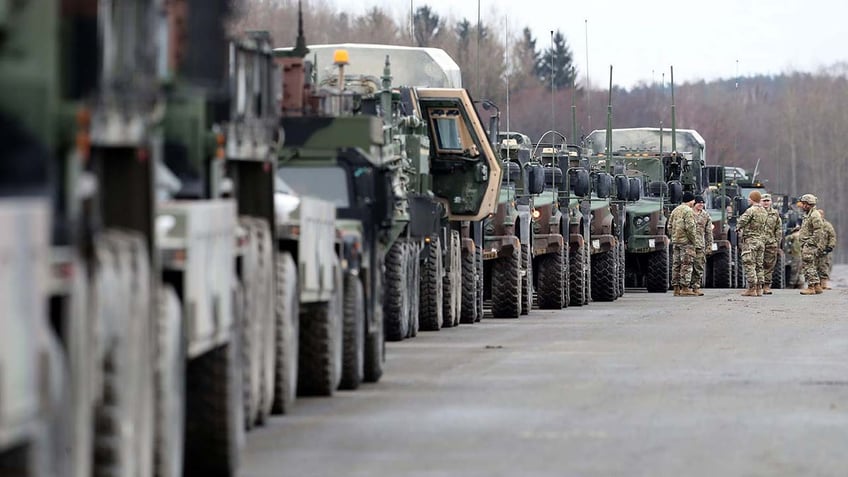 A group of soldiers stand in front of army vehicles.