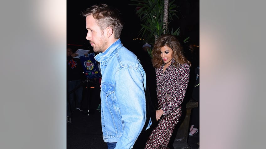 Ryan Gosling in a jean jacket leads Eva Mendes in a printed dress away from a restaurant