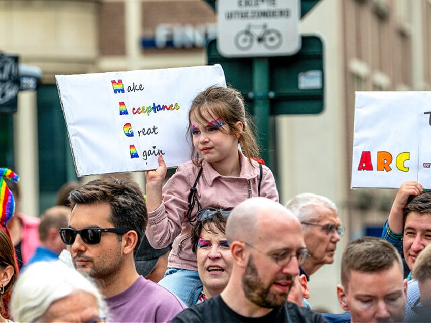 A young girl sits on someone's shoulders while holding a pride-themed sign in Brussels, Be