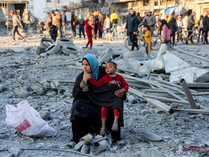 A woman sits with a child with salvaged footwear amidst debris and rubble at the site of I