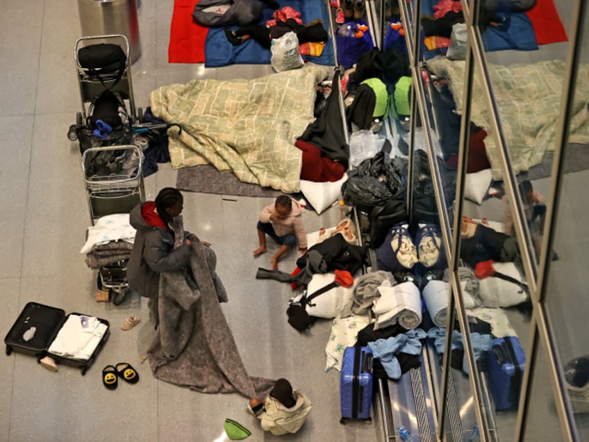 Boston, MA - January 26: In the early morning a migrant mother folds up a blanket next to three children who slept on the terminal floor overnight with their belongings scattered about. Migrants are being sheltered at Logan Airport's Terminal E overnight. During the day, they are transported to welcoming centers, but they are sleeping on the floor and on benches in the airport overnight. (Photo by David L. Ryan/The Boston Globe via Getty Images)