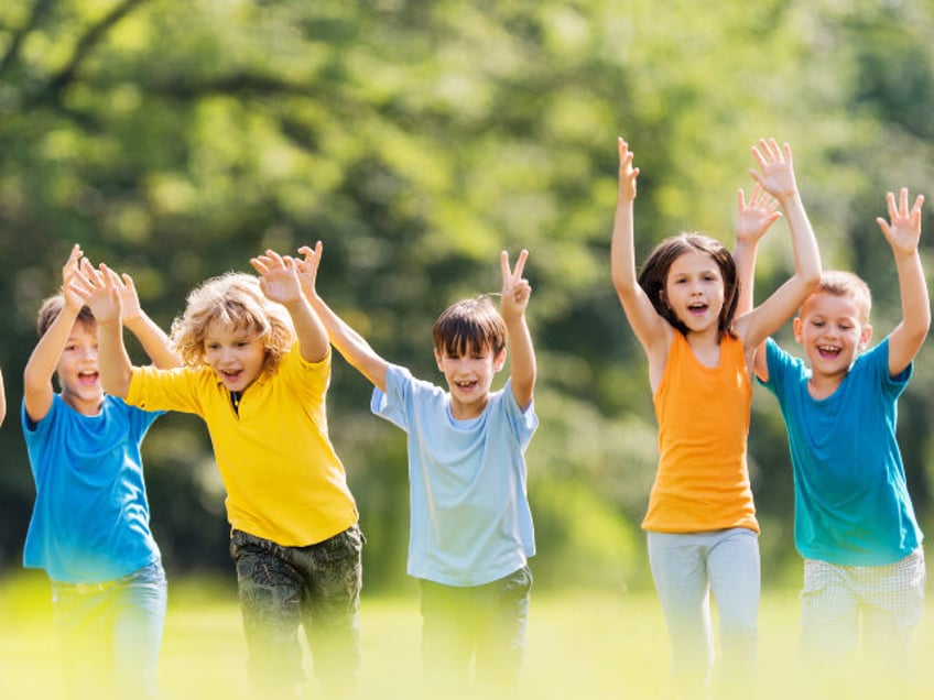 Large group of cheerful boys and girls running in nature with their hands raised.