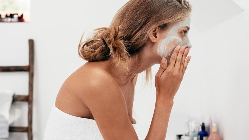 Side view shot of young woman applying facial cosmetic mask in bathroom. Female taking care of her face skin.