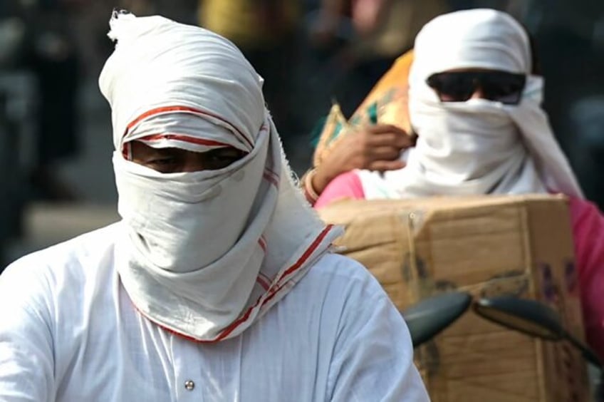 People riding bikes cover their faces with cloth on a hot summer afternoon in Varanasi on