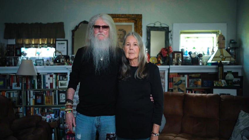 Jack Truitt posing with his wife Jackie Truitt as they wear matching black sweaters at home.