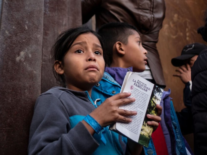 A Central American migrant girl holds a book as other migrants travelling in a caravan, cl