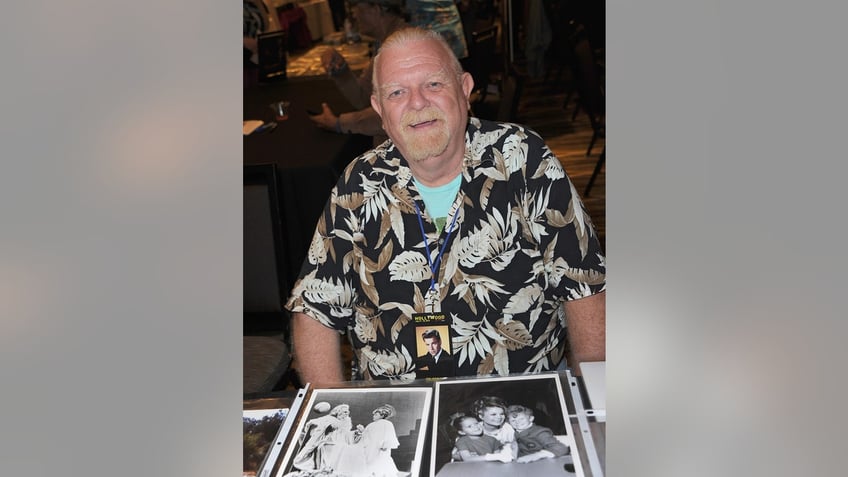 Johnny Whitaker sitting in front of several black and white photographs