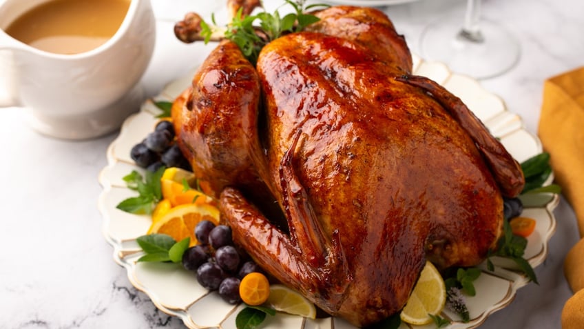 A holiday turkey sits on a platter next to a gravy dish.