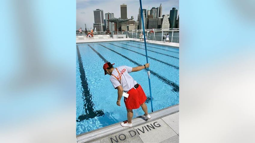 A lifeguard cleans the water at a swimming pool located on a barge anchored on Brooklyn's waterfront.