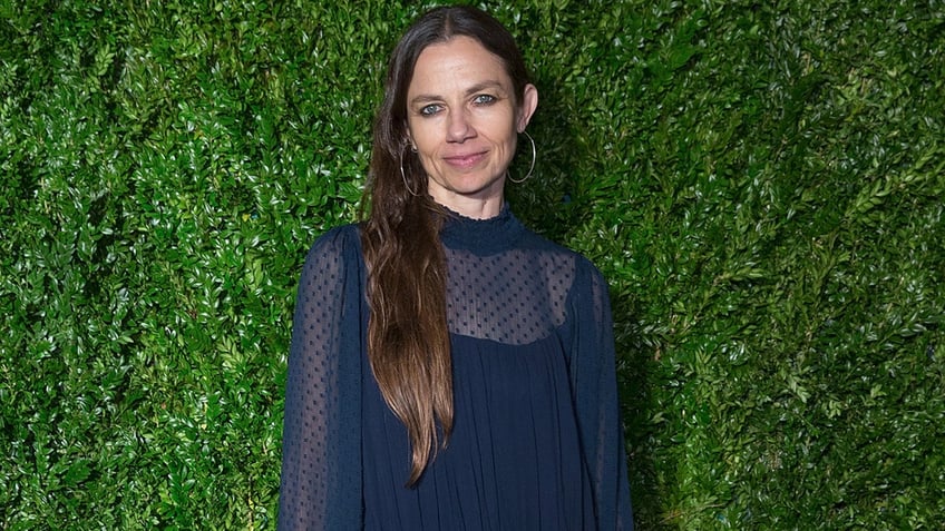 Justine Bateman smiling against a green plant backdrop