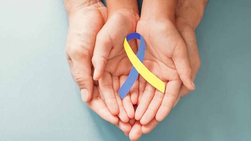 Adult and child hands holding blue and yellow ribbon for Down syndrome awareness