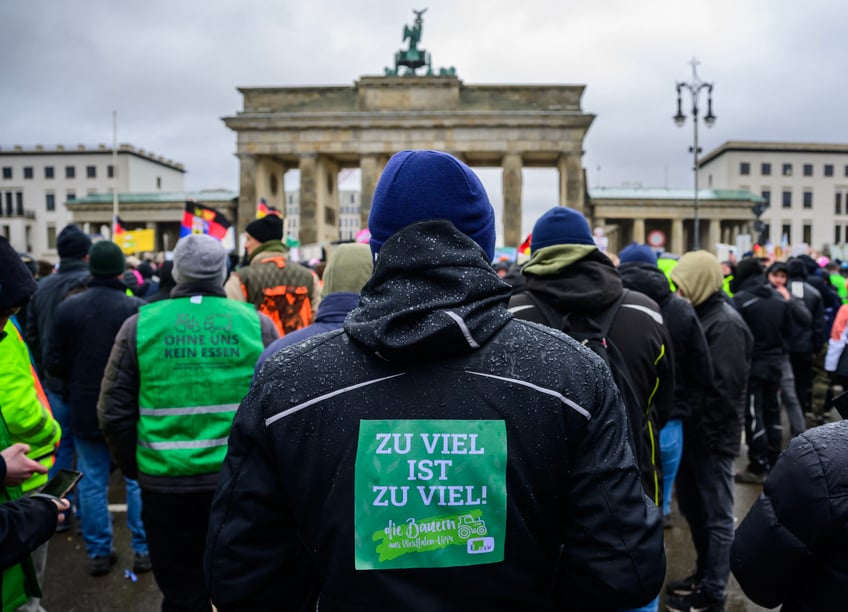 A demonstrator wears a sticker on his jacket reading: "Too much is too much" in front of Berlin's landmark Brandenburg Gate during a protest of farmers and truck drivers, on January 15, 2024 in Berlin. The farmers' and truck drivers' anger stems from a government decision to cut subsidies and tax breaks on diesel and agricultural vehicles. The move was part of efforts by German Chancellor Olaf Scholz's coalition to find savings after Germany's top court ruled in November 2023 that the government had broken debt rules. (Photo by John MACDOUGALL / AFP) (Photo by JOHN MACDOUGALL/AFP via Getty Images)