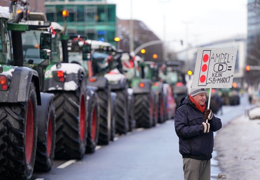 08 January 2024, Hamburg: A participant holds up a poster reading "Traffic light: D = No self-service market" in front of tractors after a rally in the city center as part of the farmers' association's week of action. In response to the federal government's austerity plans, the farmers' association has called for a week of action with rallies and rallies starting on January 8. It is to culminate in a major demonstration in the capital on January 15. Photo: Marcus Brandt/dpa (Photo by Marcus Brandt/picture alliance via Getty Images)