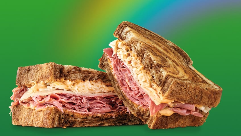 Arby's corned beef Reuben sandwich is pictured with a green background and a rainbow behind it.