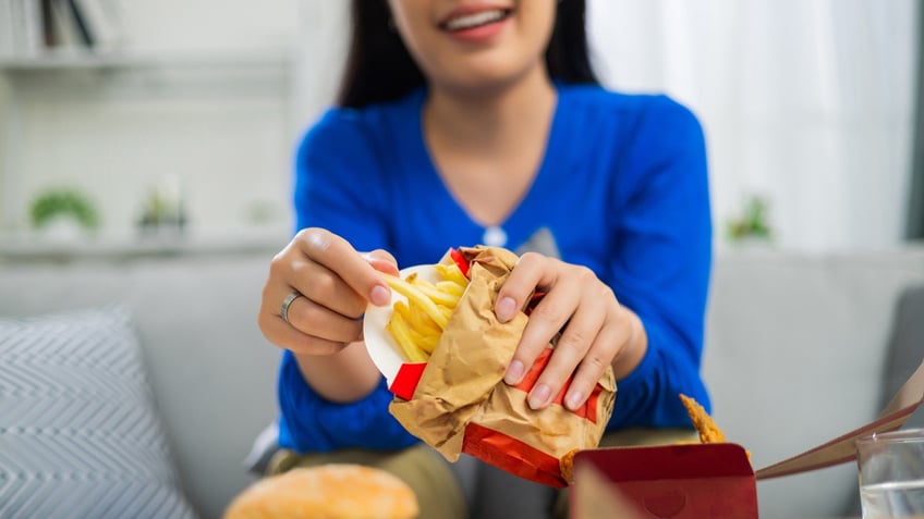 A woman smiles as she holds some fast-food fries in a bag.