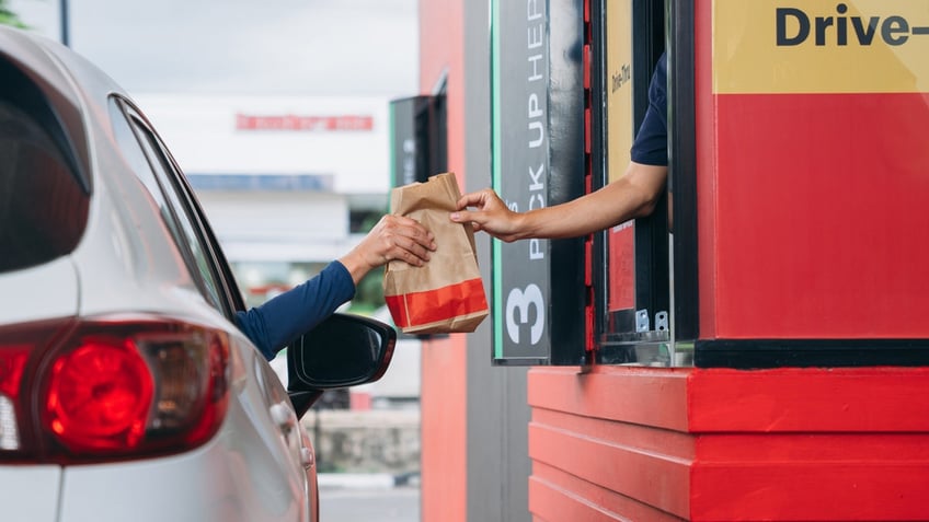 A person receives a bag of food at the drive-thru window.