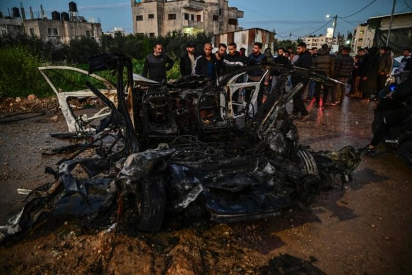 Palestinian men surround a charred car hit in an Israeli air strike on Jenin