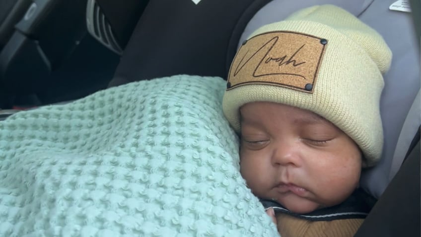 baby noah sleeping with a knitted cap that has his name written on it and a blue blanket