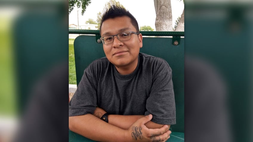 Zachariah Shorty wearing glasses and a gray t-shirt while sitting on a green bench