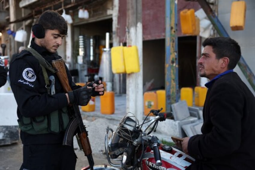 Security forces under Syria's new authorities check the identification of a man in Homs