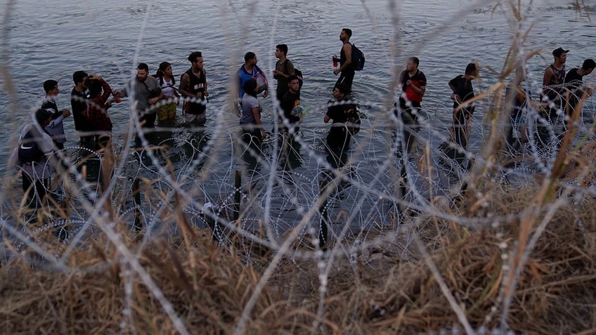 Migrants in a river, barbed wire