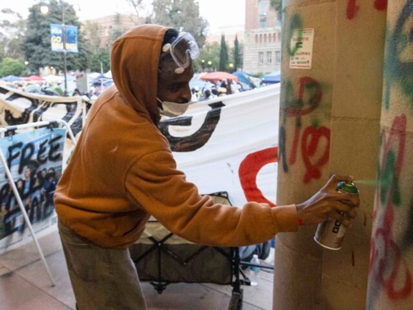 A demonstrator sprays graffiti on a building on the UCLA campus, Wednesday, May 1, 2024, i