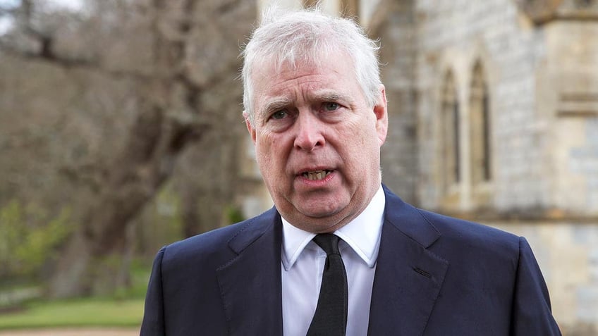 Prince Andrew in a black suit and tie walks forward with his mouth slightly ajar