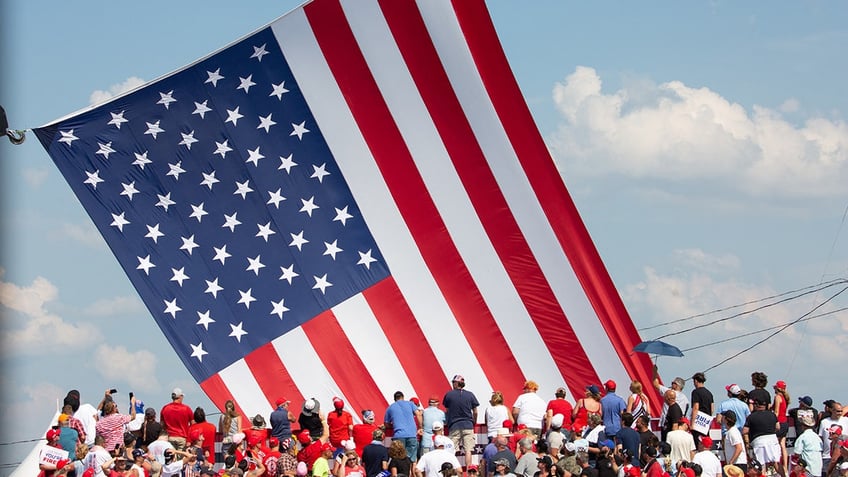 Trump supporters cheers as the American flag is untangled before former US President and Republican presidential candidate Donald Trump speaks during a campaign event