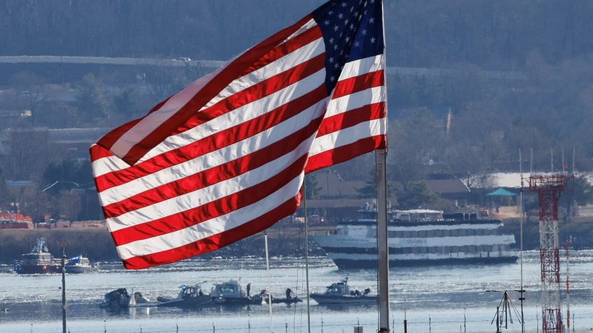 A U.S. flag flies, as search and rescue teams work, in the aftermath of the collision of American Eagle Flight 5342 and a Black Hawk helicopter that crashed into the Potomac River in Arlington, Virginia, on Jan. 30, 2025.