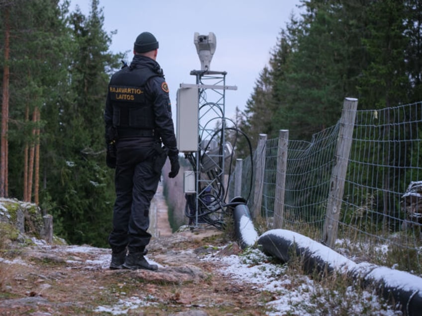 Senior border guard officer Juho Pellinen stands along a fence marking the boundary betwee