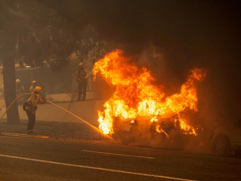 A firefighter works to extinguish a vehicle on fire on Sunset Boulevard during the Palisad