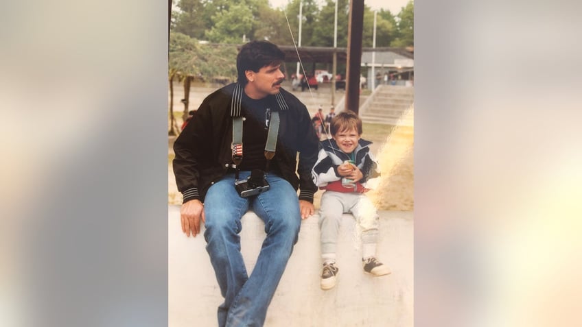 Ken Tekiela wearing jeans and a black jacket sitting next to a young Kyle laughing.