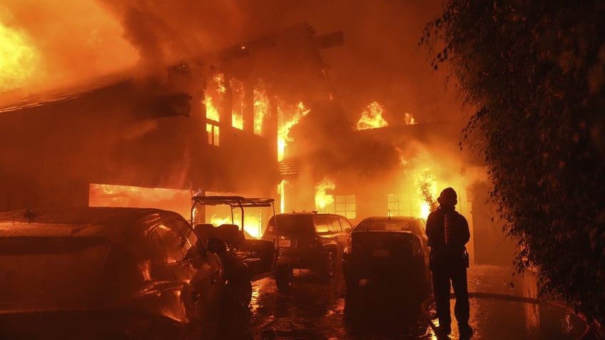 Firefighter spraying water on house in flames