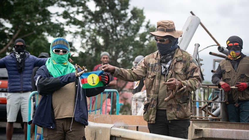 Bystanders hold a flag of the Socialist Kanak National Liberation Front on a roadblock in Ducos, New Caledonia