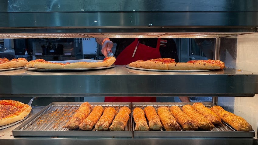 A Costco food court employee reaches for a slice of pepperoni pizza.